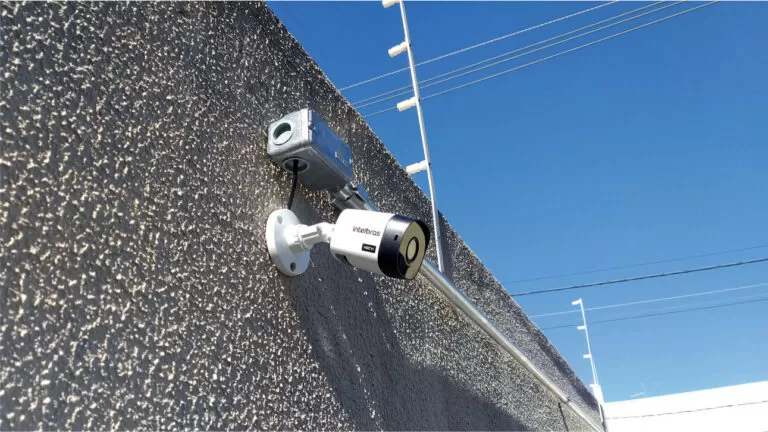 Câmera IP de segurança instalada em parede ao lado de caixa de passagem branca