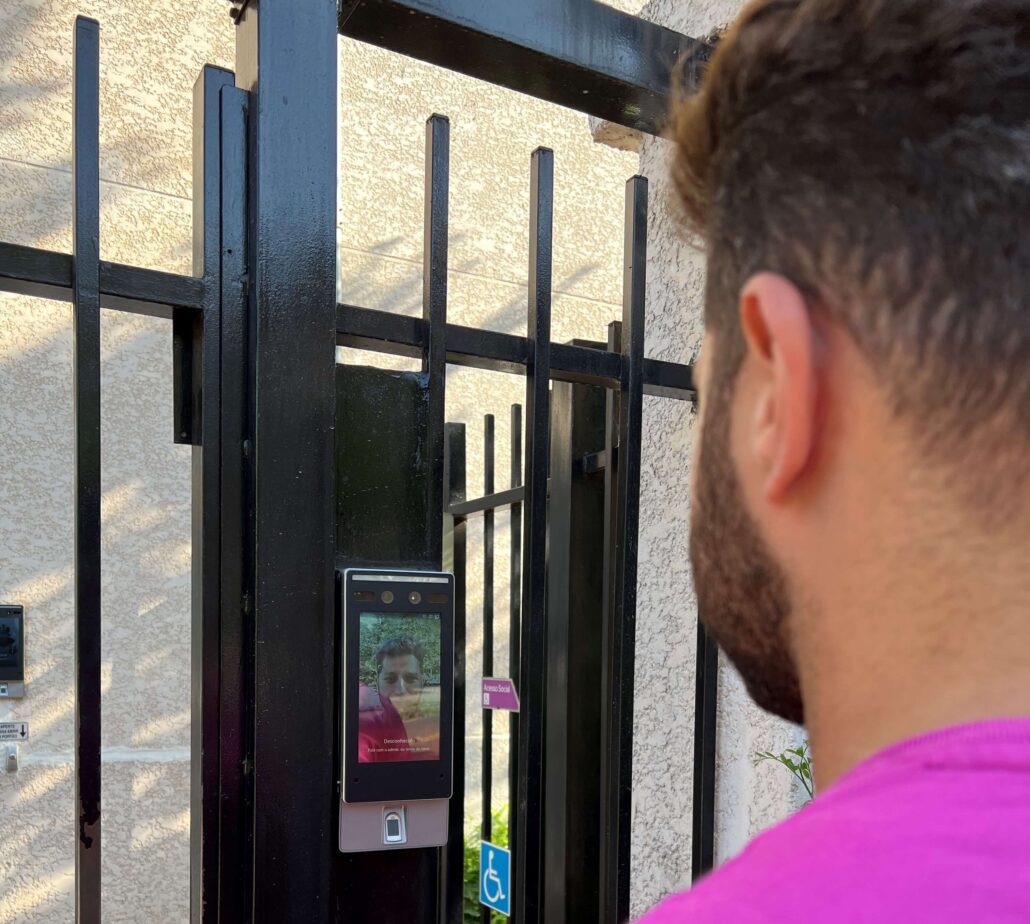 Pessoa validando acesso no terminal de reconhecimento facial com leitor de digital instalado em portão